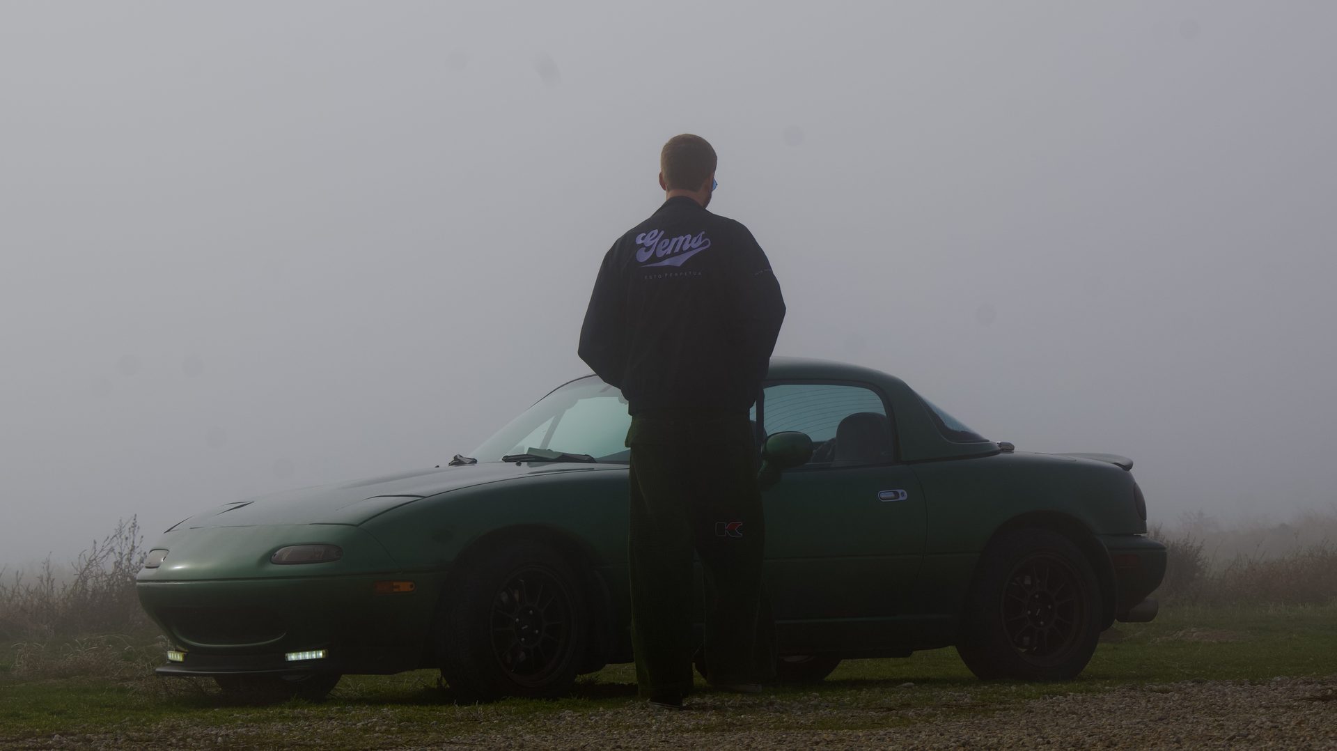 Man standing beside a Mazda Miata in the fog